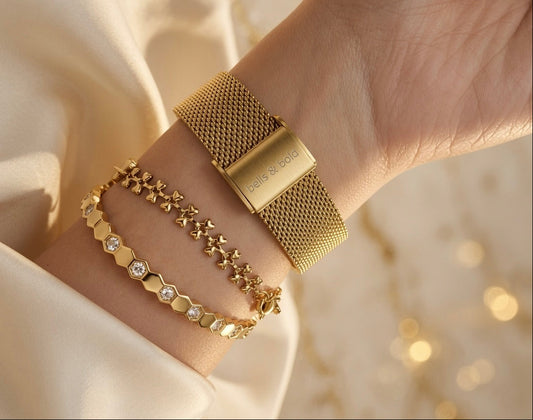 Gold bracelet watch with mesh design and star-shaped charm on a blurred beige background