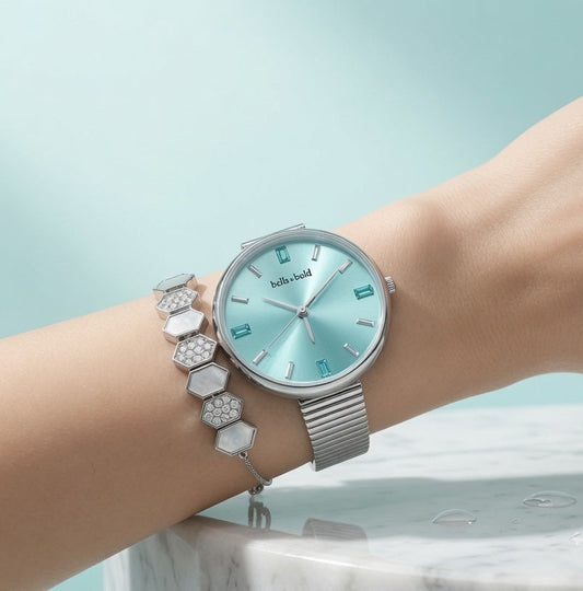 Silver watch with a turquoise face on a wrist against a light blue background